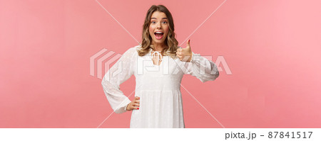 Great idea. Upbeat, enthusiastic blond caucasian girl in white spring dress, hear good plan, show thumbs-up and nod in approval, agree and recommend, satisfied with choice, stand pink background 87841517