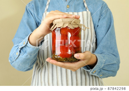 Woman in apron holds jar of pickled tomatoes Woman in apron holds jar of pickled tomatoes 87842298