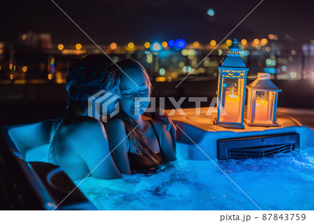 Portrait of young carefree happy smiling couple relaxing at hot tub during enjoying happy traveling moment vacation life against the background of green big mountains at night Portrait of young carefree happy smiling couple relaxing at hot tub during enjoying happy traveling moment vacation life against the background of green big mountains at night 87843759
