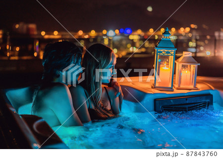 Portrait of young carefree happy smiling couple relaxing at hot tub during enjoying happy traveling moment vacation life against the background of green big mountains at night 87843760