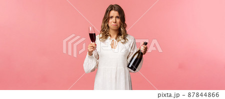 Holidays, spring and party concept. Portrait of upset and whining young blond woman being cheated trying to ease pain with alcohol, holding glass wine and bottle, grimacing want cry, complaining Holidays, spring and party concept. Portrait of upset and whining young blond woman being cheated trying to ease pain with alcohol, holding glass wine and bottle, grimacing want cry, complaining 87844866