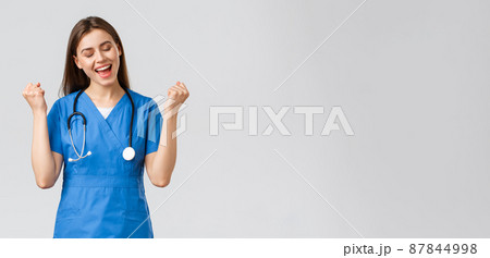 Medical workers, healthcare, covid-19 and vaccination concept. Happy cheerful female nurse, pretty enthusiastic doctor in blue scrubs, passed test, fist pump in rejoice, smiling relieved 87844998