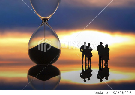 miniature people. silhouettes of different people watching the sunset next to the hourglass. 87856412