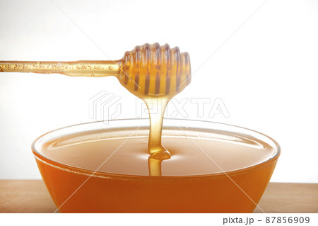 fresh honey dripping from a spoon into a transparent plate on a white background. 87856909
