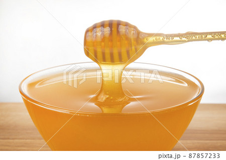 fresh honey dripping from a spoon into a transparent plate on a white background. fresh honey dripping from a spoon into a transparent plate on a white background. 87857233