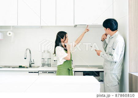 キッチンで話す作業着姿の男性と女性（換気扇・クレーム） 87860810