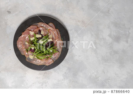 Slices of beef tenderloin, with arugula leaves, parmesan and spices. On a gray background, top view, layout with space for text. Slices of beef tenderloin, with arugula leaves, parmesan and spices. On a gray background, top view, layout with space for text. 87866640
