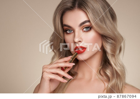 A beautiful young blonde woman applying lipstick 87867094