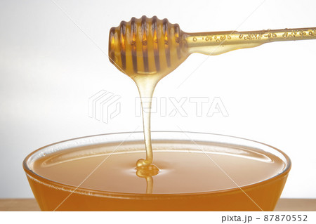 fresh honey dripping from a spoon into a transparent plate on a white background 87870552