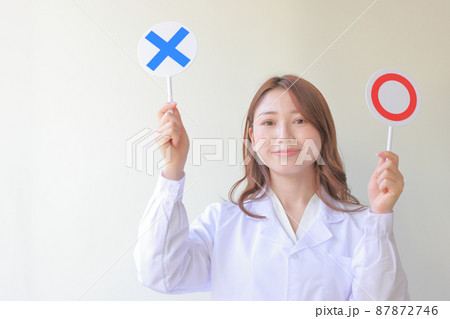 〇とXのプレートを持つにこやかな白衣女性1 〇とXのプレートを持つにこやかな白衣女性1 87872746