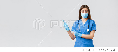 Covid-19, preventing virus, health, healthcare workers and quarantine concept. Interested and questioned female doctor, nurse in blue scrubs and medical mask, asking question pointing left Covid-19, preventing virus, health, healthcare workers and quarantine concept. Interested and questioned female doctor, nurse in blue scrubs and medical mask, asking question pointing left 87874178