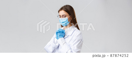 Covid-19, preventing virus, health, healthcare workers and quarantine concept. Doctor in medical mask and scrubs praying god, believe in Lord, asking cure coronavirus disease, grey background Covid-19, preventing virus, health, healthcare workers and quarantine concept. Doctor in medical mask and scrubs praying god, believe in Lord, asking cure coronavirus disease, grey background 87874252