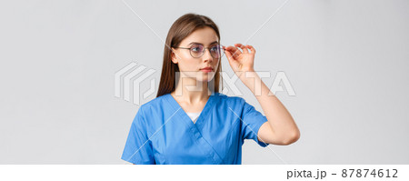 Healthcare workers, medicine, insurance and covid-19 pandemic concept. Professional young smart doctor or nurse, female intern in scrubs and glasses, looking right at banner serious face 87874612