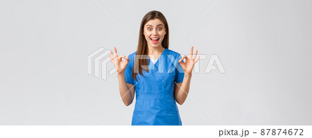 Healthcare workers, prevent virus, insurance and medicine concept. Enthusiastic cheerful nurse, doctor in blue scrubs show okay sign in approval, guarantee quality, recommend service 87874672