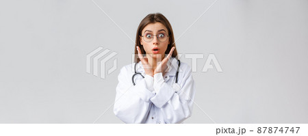 Healthcare workers, medicine, insurance and covid-19 pandemic concept. Surprised and impressed female doctor in glasses, white scrubs, gasping and staring astonished camera, grey background Healthcare workers, medicine, insurance and covid-19 pandemic concept. Surprised and impressed female doctor in glasses, white scrubs, gasping and staring astonished camera, grey background 87874747