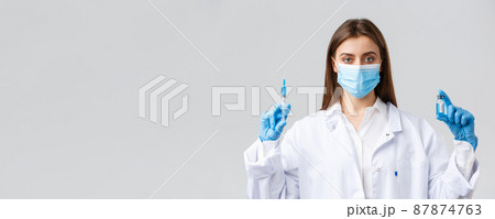 Covid-19, preventing virus, healthcare workers and quarantine concept. Doctor in personal protective equipment, medical mask and scrubs making coronavirus vaccine shot, hold syringe and ampoule Covid-19, preventing virus, healthcare workers and quarantine concept. Doctor in personal protective equipment, medical mask and scrubs making coronavirus vaccine shot, hold syringe and ampoule 87874763
