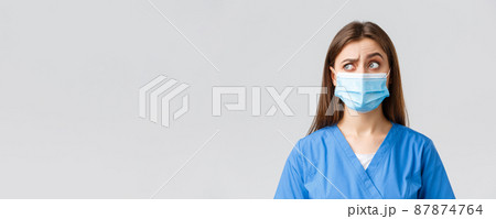 Covid-19, preventing virus, healthcare workers and quarantine concept. Skeptical female nurse or doctor in blue scrubs, medical mask, raise one eyebrow intrigued and confused, look upper left corner Covid-19, preventing virus, healthcare workers and quarantine concept. Skeptical female nurse or doctor in blue scrubs, medical mask, raise one eyebrow intrigued and confused, look upper left corner 87874764
