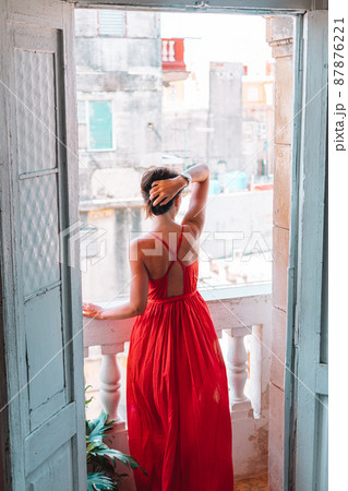 Young attractive woman in red dress on old balcony in apartment in Havana Young attractive woman in red dress on old balcony in apartment in Havana 87876221