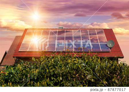Photo collage of solar panels, photovoltaics on the red roof of a house and a beautiful sky with the setting sun. Alternative electricity source. Concept of sustainable resources 87877017