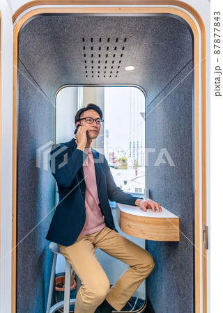 フリーアドレスオフィスの防音電話ボックスで電話をする男性 フリーアドレスオフィスの防音電話ボックスで電話をする男性 87877843