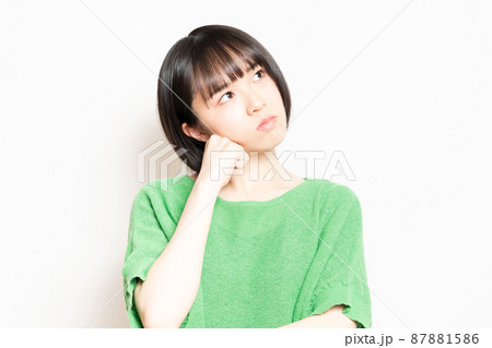 白い背景の前に立って悩んでいる緑の服を着ている若い女性 87881586