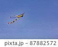 A kite painted in the colors of a rainbow flies against the background of a blue sky. 87882572