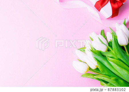 Mothers day gift. Spring white tulip flower, gift with red ribbon on flat lay pink background. Valentines, birthday, women or wedding day concept. 87883102
