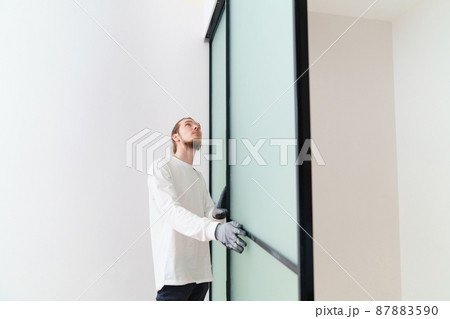 master adjusts sliding doors of wardrobe made of metal and glass. 87883590