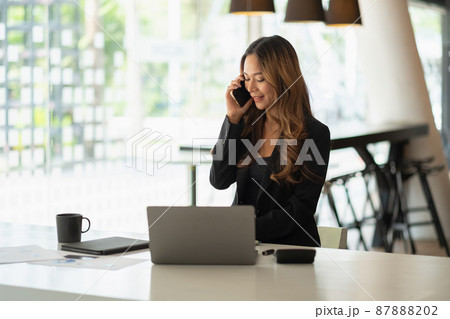 Young chariming asian woman using her laptop while call phone and sitting at her working place. 87888202