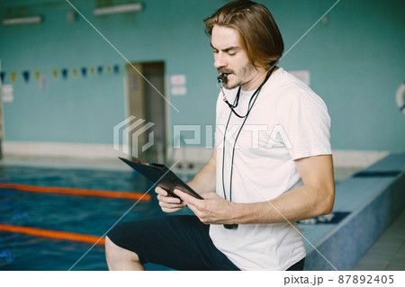 Serious trainer holding clipboard and blowing whistle Serious trainer holding clipboard and blowing whistle 87892405