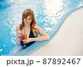 Young girl in a swimwear relaxing in a pool and holding a cocktail 87892467