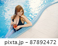 Young girl in a swimwear relaxing in a pool and holding a cocktail 87892472