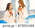 Two girls in a dressing gowns relaxing in a spa and holding a cocktails 87892488