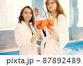 Two girls in a dressing gowns relaxing in a spa and holding a cocktails 87892489
