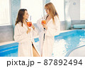 Two girls in a dressing gowns relaxing in a spa and holding a cocktails 87892494