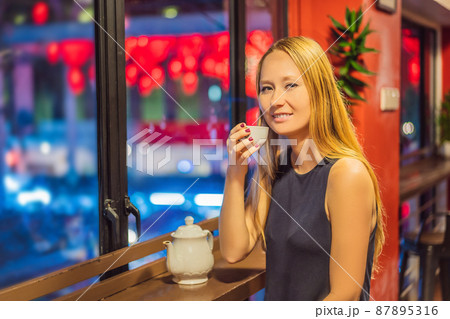 A young woman drinks Chinese tea on a background of red Chinese lanterns in honor of the Chinese New Year 87895316