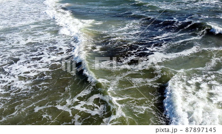 Aerial drone view flight over sea waves that roll onto sandy shore. 87897145