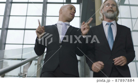 two corporate executives talking while descending stairs in modern office building 87897884