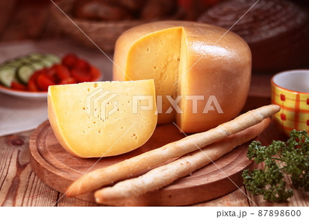 yellow loaf of hard cheese on a chopping board 87898600