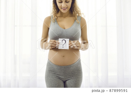 Smiling healthy pregnant woman hold paper with question mark sign wonder about baby sex. Happy girl excited with pregnancy think of newborn kid gender. Ultrasound screening, motherhood. Smiling healthy pregnant woman hold paper with question mark sign wonder about baby sex. Happy girl excited with pregnancy think of newborn kid gender. Ultrasound screening, motherhood. 87899591