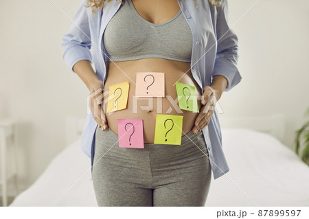 Choosing baby name. Cropped image of pregnant woman with many colored stickers on her abdomen showing question marks. Woman wants to choose name and know sex of her unborn child. Expectancy concept. 87899597