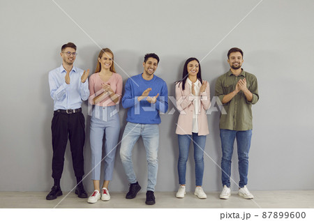 Friendly and happy young successful people stand in line and applaud their leader. Variety of casual young people standing in row near wall are smiling and proudly applauding without looking at camera Friendly and happy young successful people stand in line and applaud their leader. Variety of casual young people standing in row near wall are smiling and proudly applauding without looking at camera 87899600