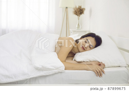 Happy tranquil beautiful woman napping lying on comfortable bedding in bedroom at home alone. Side view of smiling caucasian woman enjoying resting. Refreshment, renew energy and strength concept. Happy tranquil beautiful woman napping lying on comfortable bedding in bedroom at home alone. Side view of smiling caucasian woman enjoying resting. Refreshment, renew energy and strength concept. 87899675