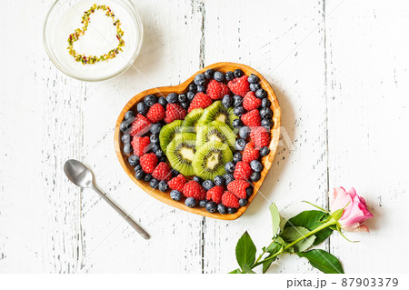 S.Valentine's Day breakfast concept. Mix of berries and kiwi in a heart shaped bowl, yogurt with pistachios and rose S.Valentine's Day breakfast concept. Mix of berries and kiwi in a heart shaped bowl, yogurt with pistachios and rose 87903379