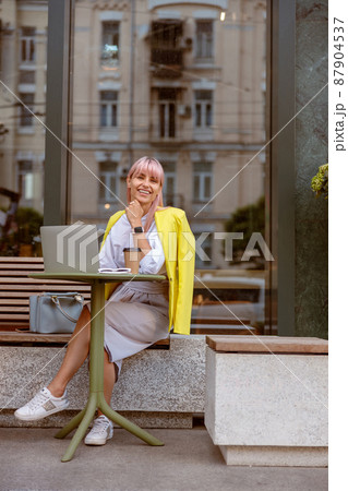 Cheerful woman sitting at the table with laptop on the street Cheerful woman sitting at the table with laptop on the street 87904537