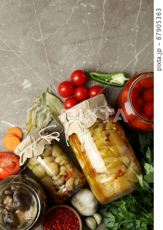 Jars of pickled vegetables and ingredients on gray textured table Jars of pickled vegetables and ingredients on gray textured table 87905363