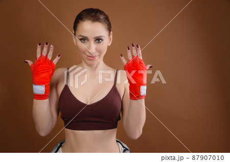 Attractive young caucasian woman with training bandages on her hands stands showing her hands. Studio portrait. brown background 87907010