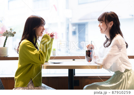 カフェの窓のそばの席に座り話をしている2人の若い女性の写真素材