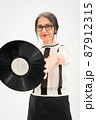 Studio photo of middle aged woman starting getting grey-haired wearing black and white clothes with vinyl record in hands on white background, middle age sexy lady, happy life concept 87912315