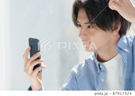 スマホで髪型をチェックする若い男性 スマホで髪型をチェックする若い男性 87917324